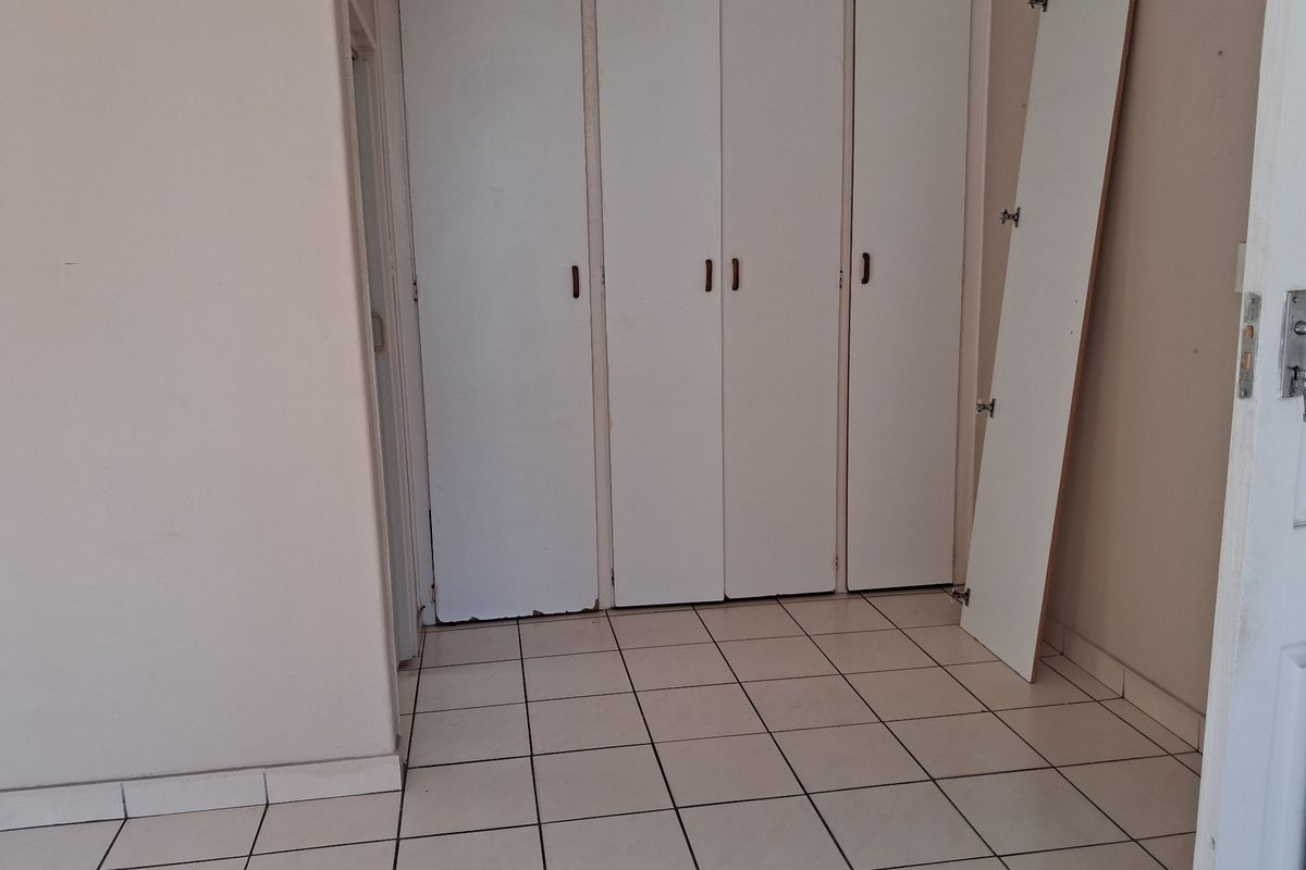 An empty bedroom featuring tiled flooring and built-in cupboards with visible wear and a detached cupboard door panel.