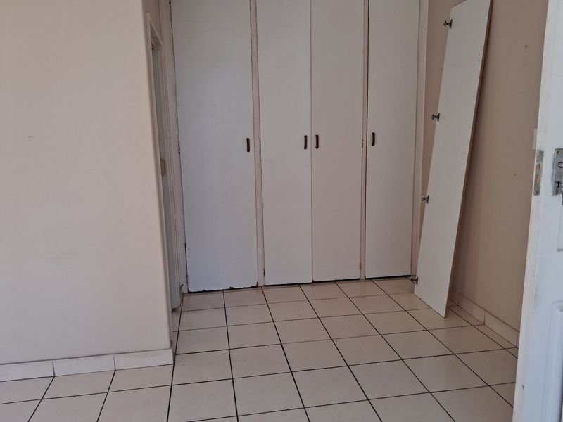 An empty bedroom featuring tiled flooring and built-in cupboards with visible wear and a detached cupboard door panel.