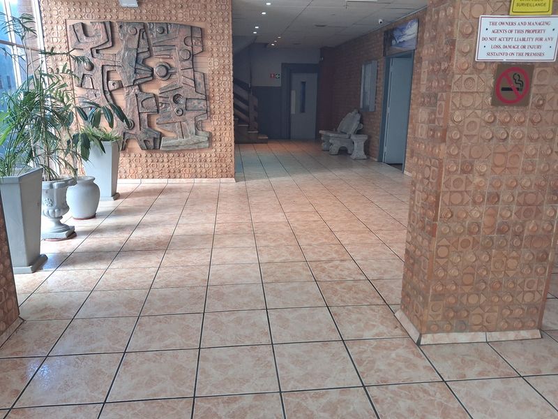 Spacious apartment building entrance lobby featuring textured brick wall detailing, ceramic floor tiles, and recessed ceiling lighting.