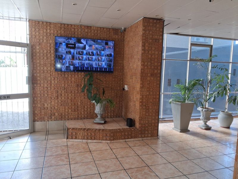 Entrance lobby area featuring tiled flooring, a textured feature wall with security monitoring display, and large windows providing natural light.