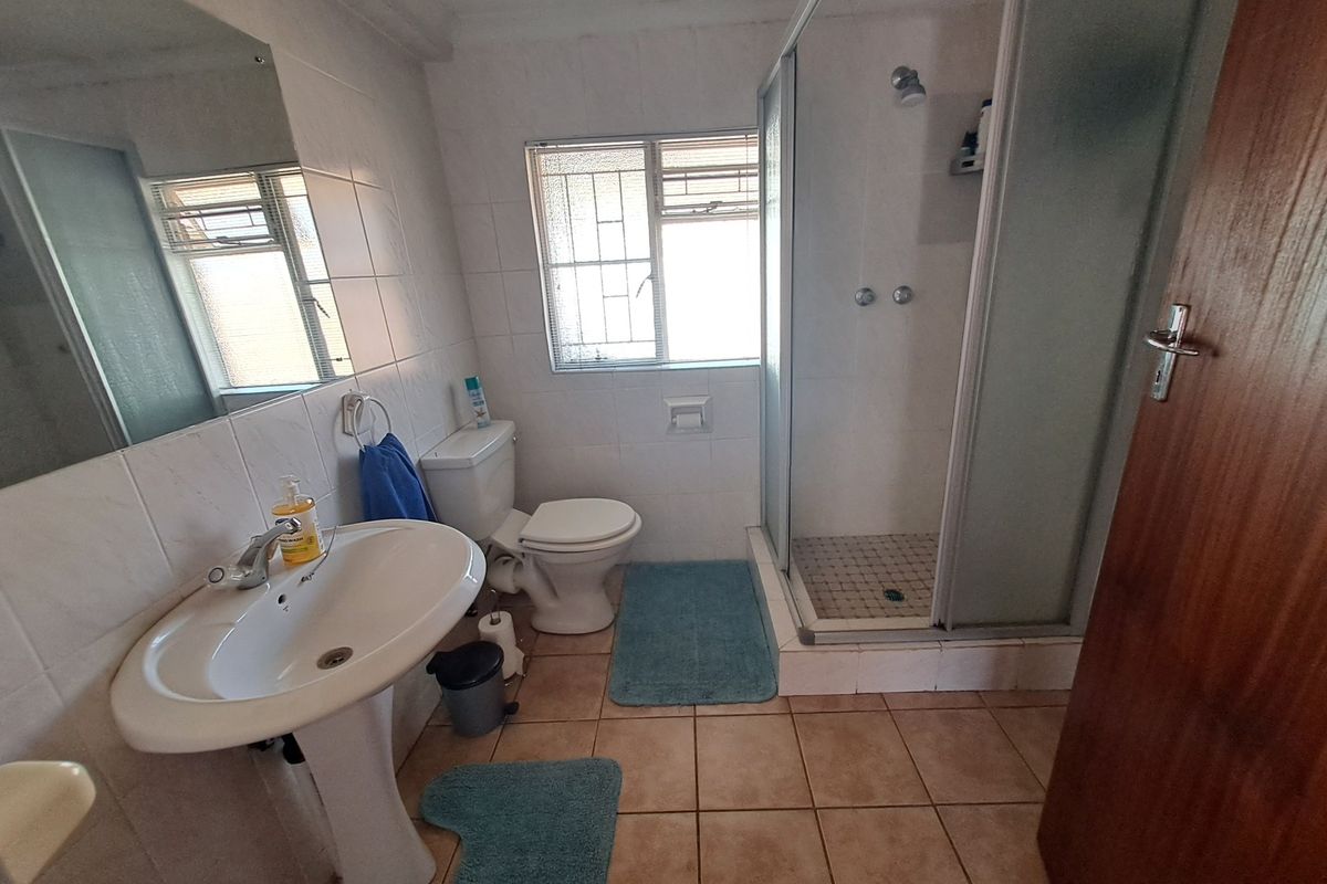 A functional bathroom featuring a pedestal basin, toilet, and a glass-enclosed shower with tiled walls and flooring.