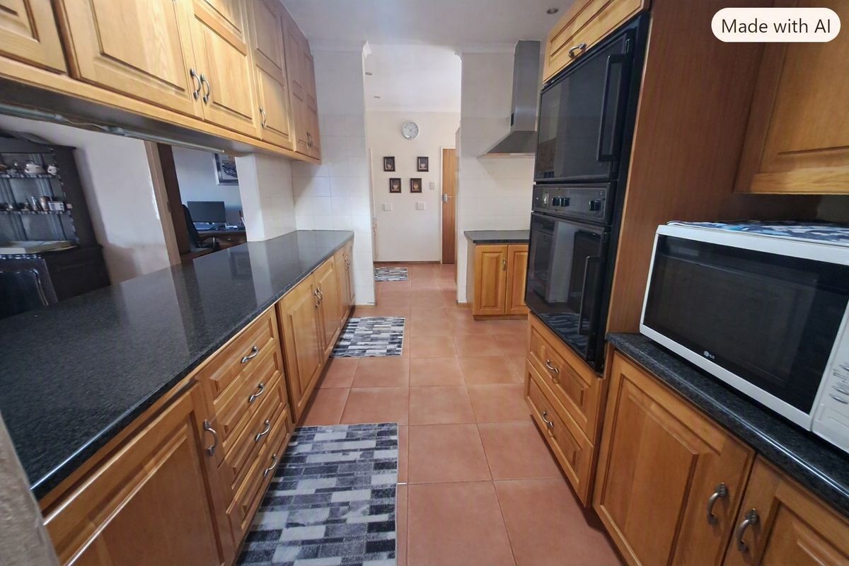 A functional kitchen featuring wooden cabinetry, granite countertops, a double wall oven, and an extractor fan, with tiled flooring throughout.