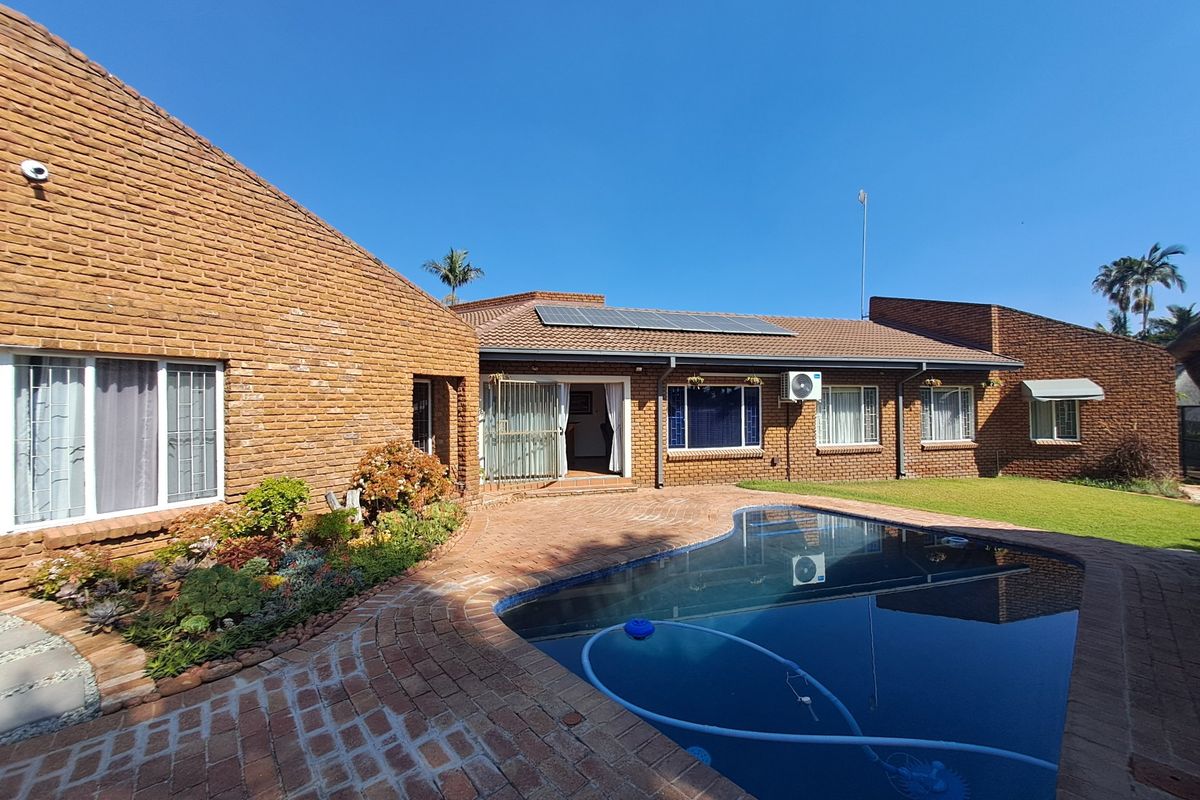 Rear exterior view featuring a brick facade, a swimming pool with paved surround, solar panels, and well-maintained garden areas.