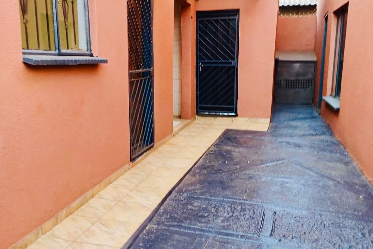 A side exterior walkway featuring tiled flooring, security gates, and a protective awning over the entrance.