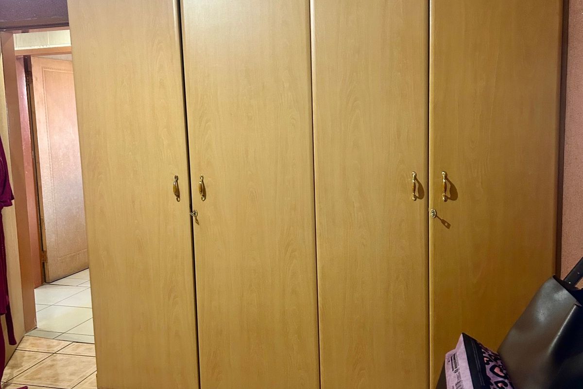 A bedroom featuring a large, light wood-finish built-in wardrobe and tiled flooring, providing ample storage space.