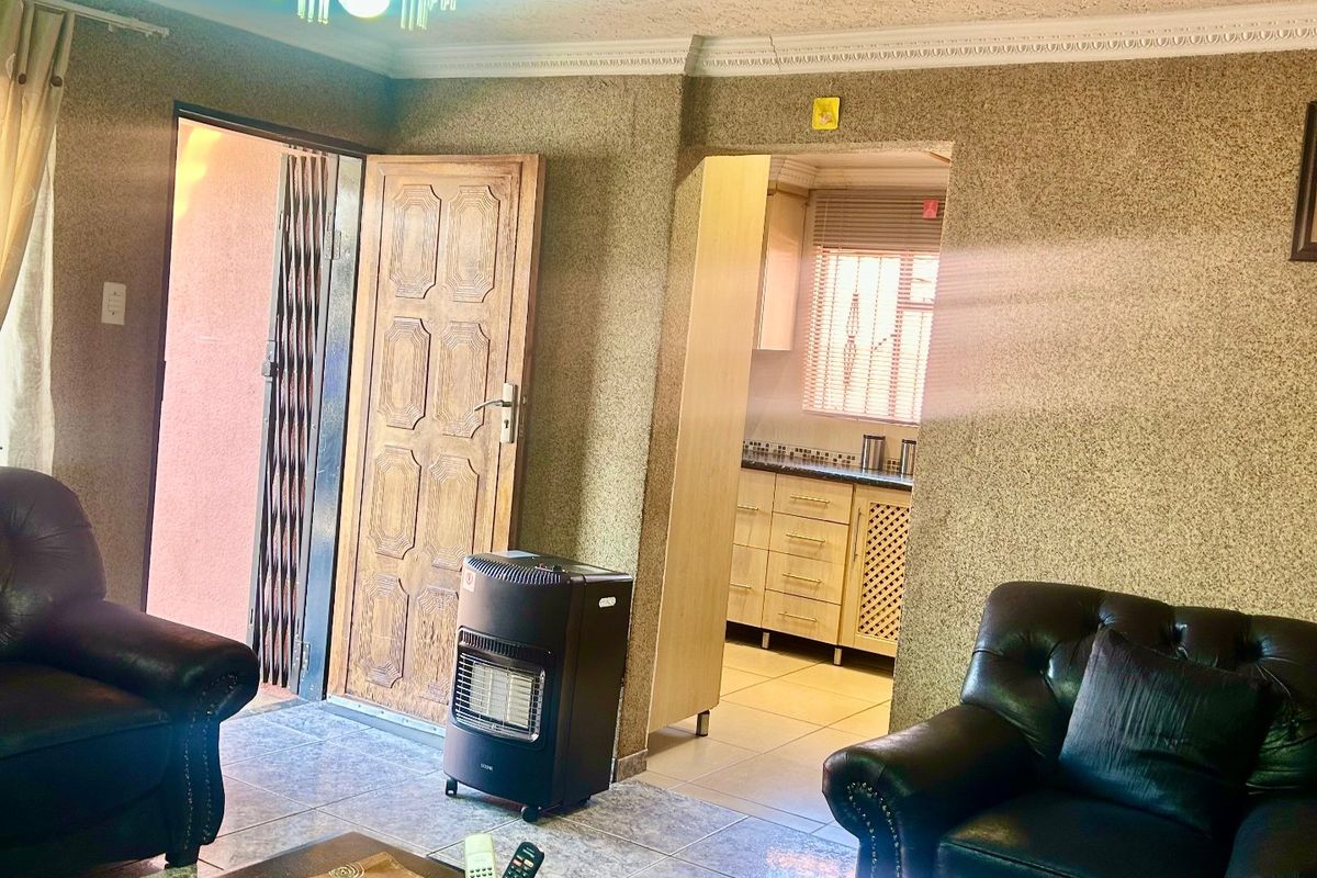 A living room featuring decorative ceiling details, tiled flooring, and direct access to an adjacent kitchen area.