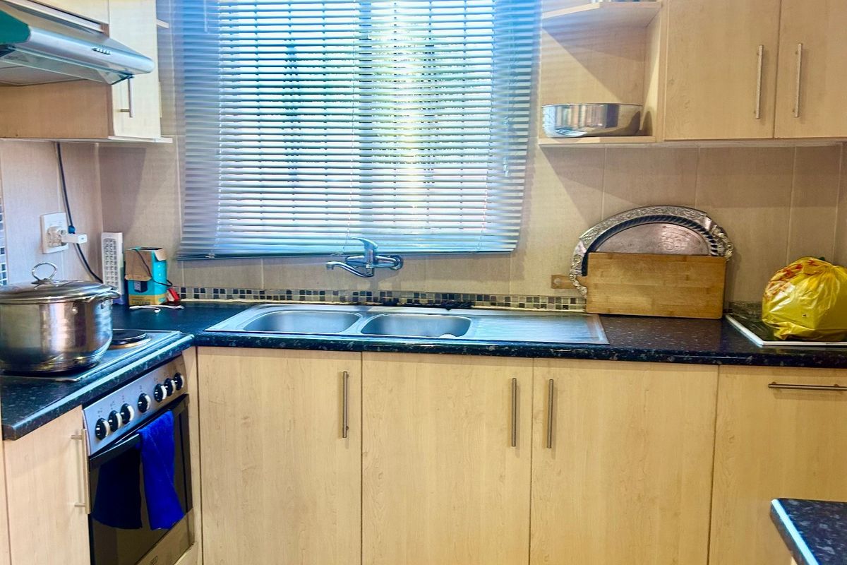 Functional kitchen featuring light wood-finish cabinetry, dark laminate countertops, a double stainless steel sink, and built-in oven with extractor fan.