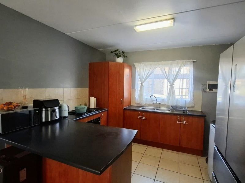 A functional kitchen featuring laminate cabinetry, dark countertops, a double basin sink, and tiled flooring, offering a practical layout for daily meal preparation.