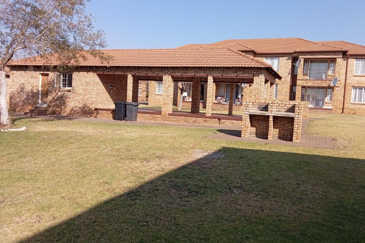 Rear view of the apartment complex featuring a communal lawn, covered patio area, and a built-in brick braai facility.