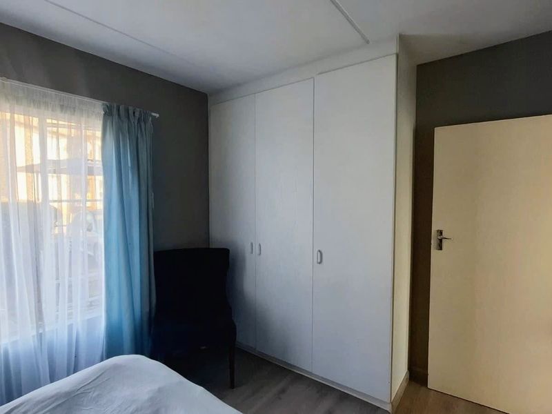 A bedroom featuring built-in cupboards and laminate flooring, offering a functional and neutral space.