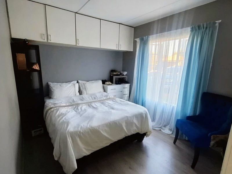 A compact bedroom featuring built-in overhead storage cabinetry and laminate flooring, providing functional space with natural light from the window.