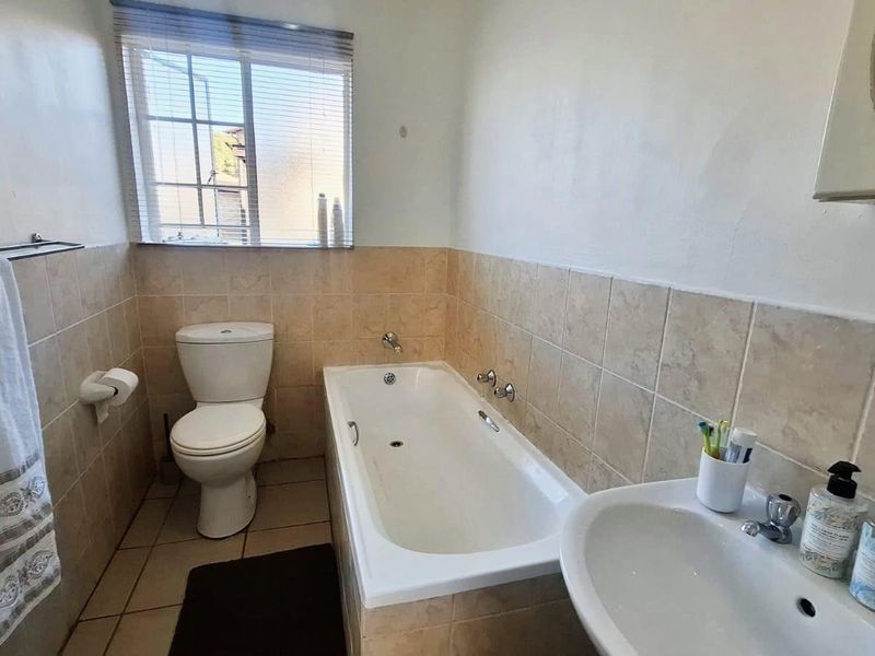 A functional bathroom featuring a bathtub, pedestal basin, and toilet with neutral wall and floor tiling, providing a clean and practical space.