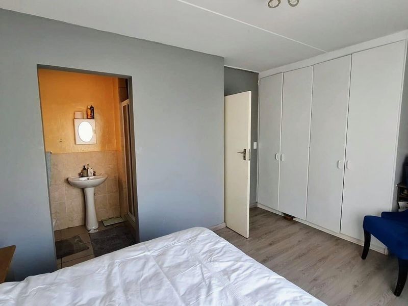 Bedroom featuring built-in cupboards, laminate flooring, and an attached en-suite bathroom with a pedestal sink.
