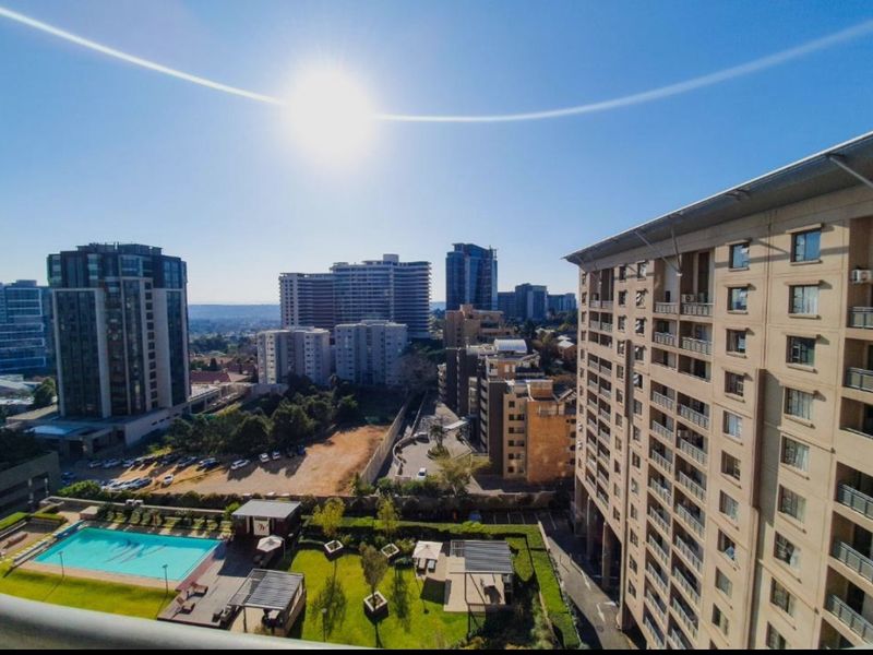Elevated urban view overlooking the apartment complex grounds, featuring a swimming pool, landscaped garden areas, and surrounding city skyline.