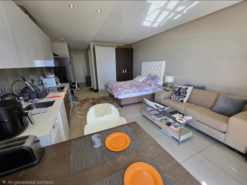 A modern open-plan studio apartment featuring a compact kitchen with built-in cabinetry, tiled flooring, and recessed lighting, seamlessly integrated with the living and sleeping area.