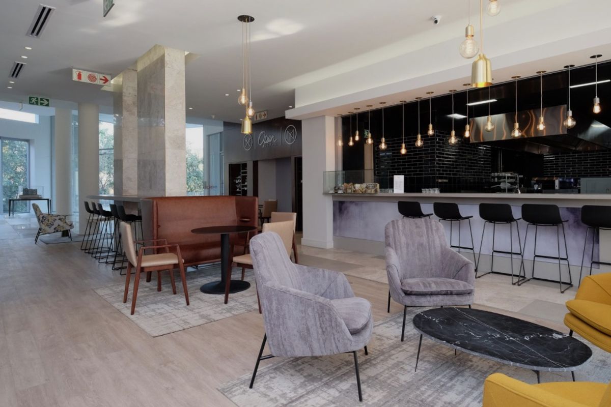 Modern open-plan communal area featuring a sleek bar with black subway tile backsplash, stone-clad architectural pillars, and contemporary recessed lighting.