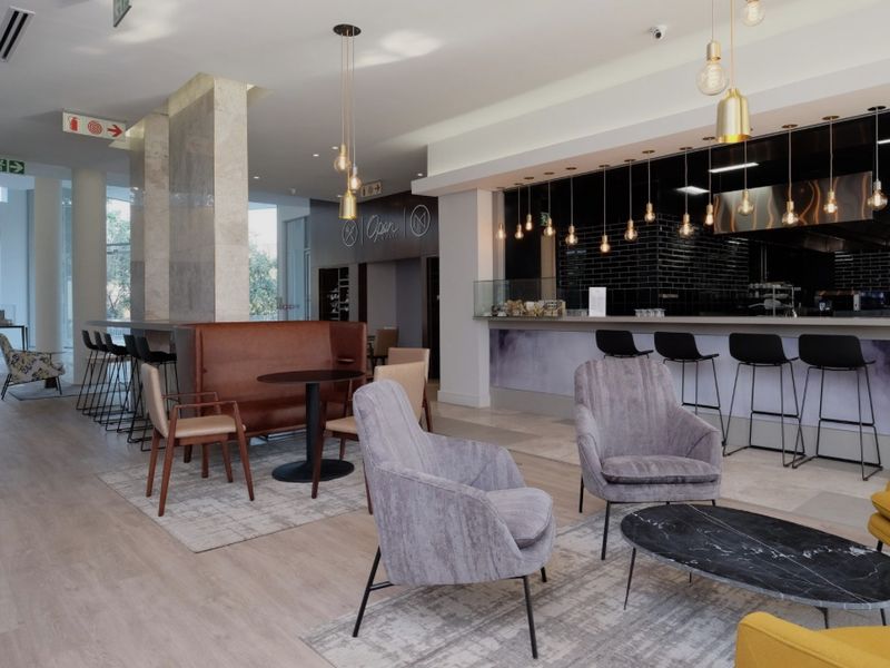 Modern open-plan communal area featuring a sleek bar with black subway tile backsplash, stone-clad architectural pillars, and contemporary recessed lighting.