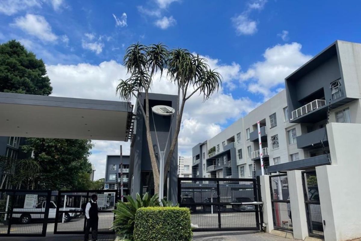 The entrance to the apartment complex features a secure gated access point with a boom gate, electric fencing, and a dedicated security guard station.