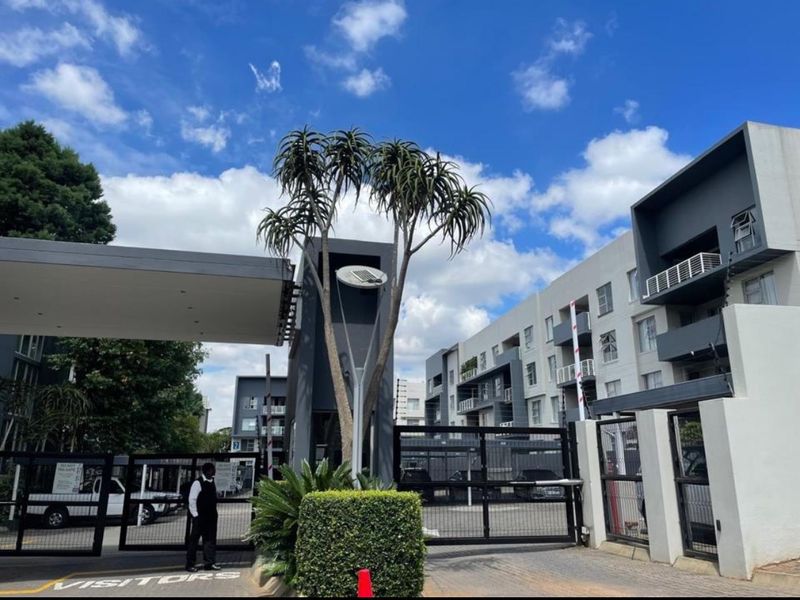 The entrance to the apartment complex features a secure gated access point with a boom gate, electric fencing, and a dedicated security guard station.