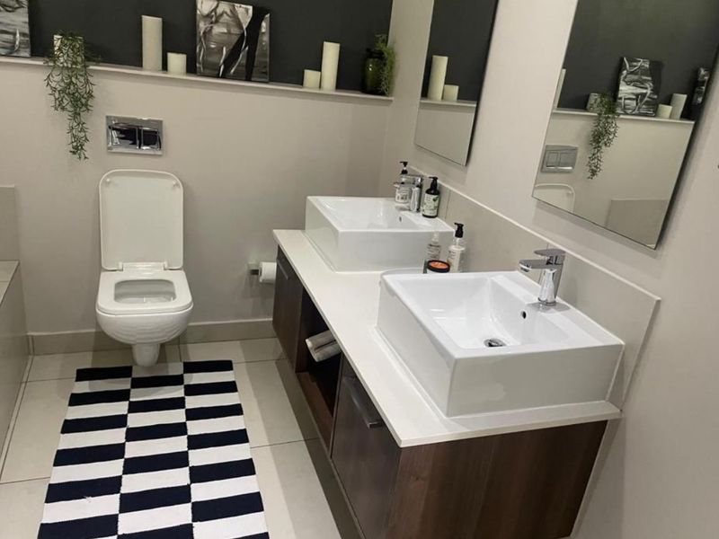 Modern bathroom featuring a double vanity with vessel sinks, wall-mounted toilet, and clean tiled finishes.