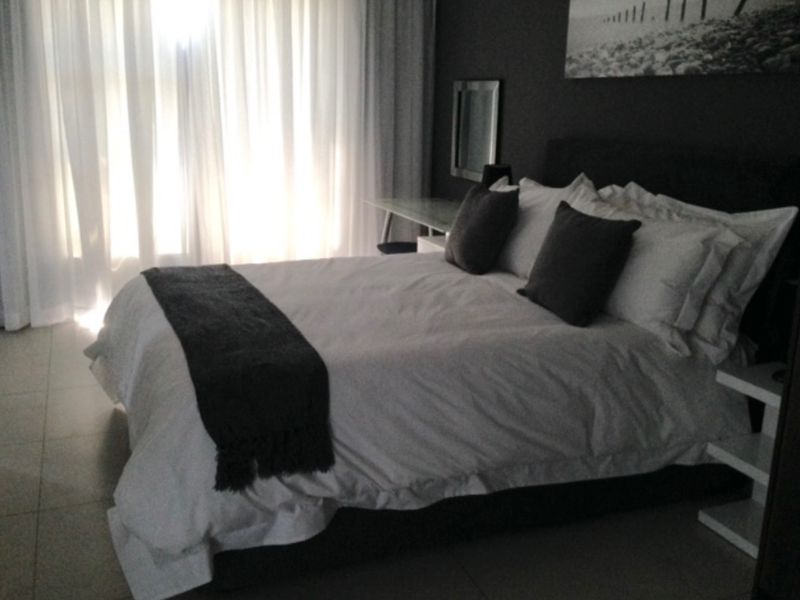 A modern bedroom featuring tiled flooring and floor-to-ceiling sheer curtains, creating a bright and comfortable sleeping space.