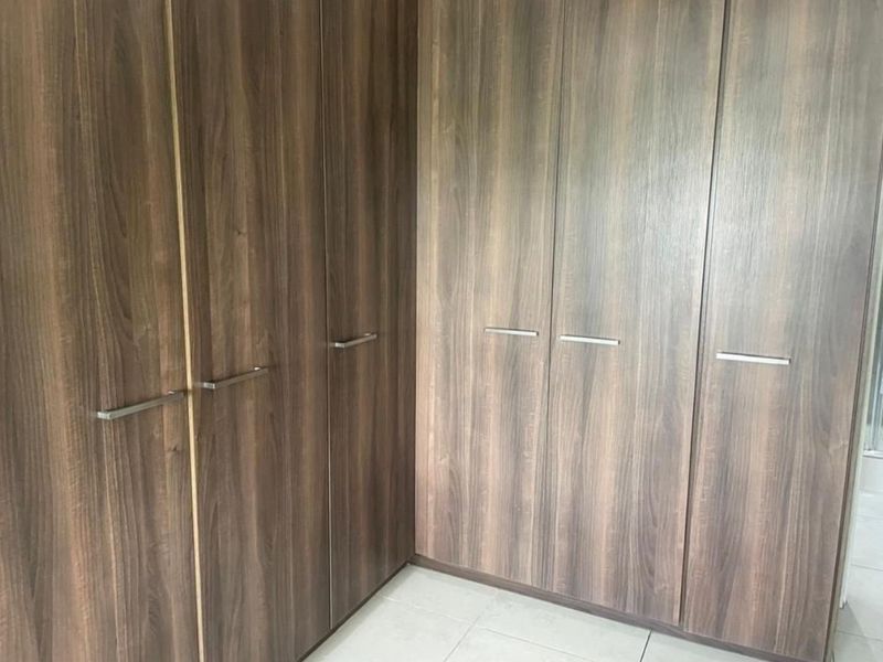 A bedroom featuring modern, full-height built-in wooden cupboards and neutral tiled flooring.