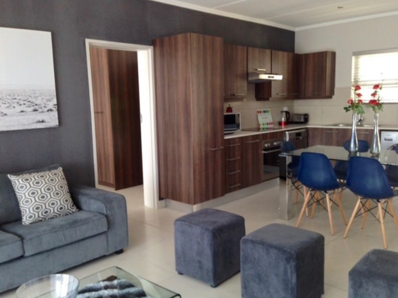 Open-plan living area featuring a modern kitchen with dark wood cabinetry, integrated appliances, and tiled flooring, seamlessly connecting to the lounge space.