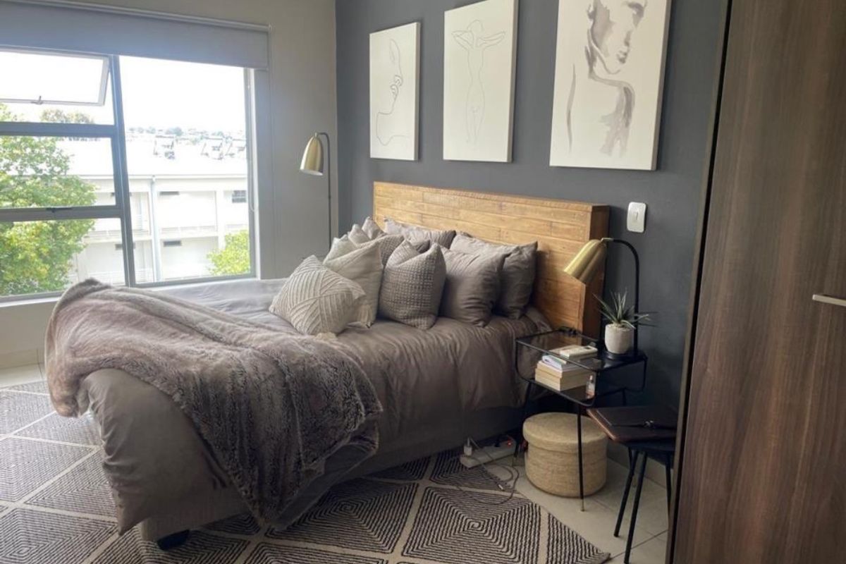 A well-maintained bedroom featuring a large window with a roller blind, a dark accent wall, and a built-in wardrobe.