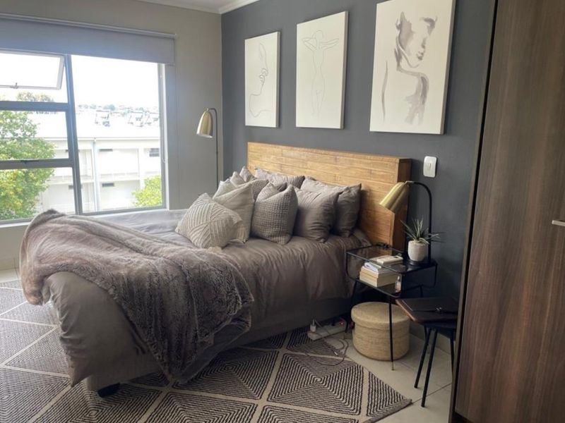 A well-maintained bedroom featuring a large window with a roller blind, a dark accent wall, and a built-in wardrobe.