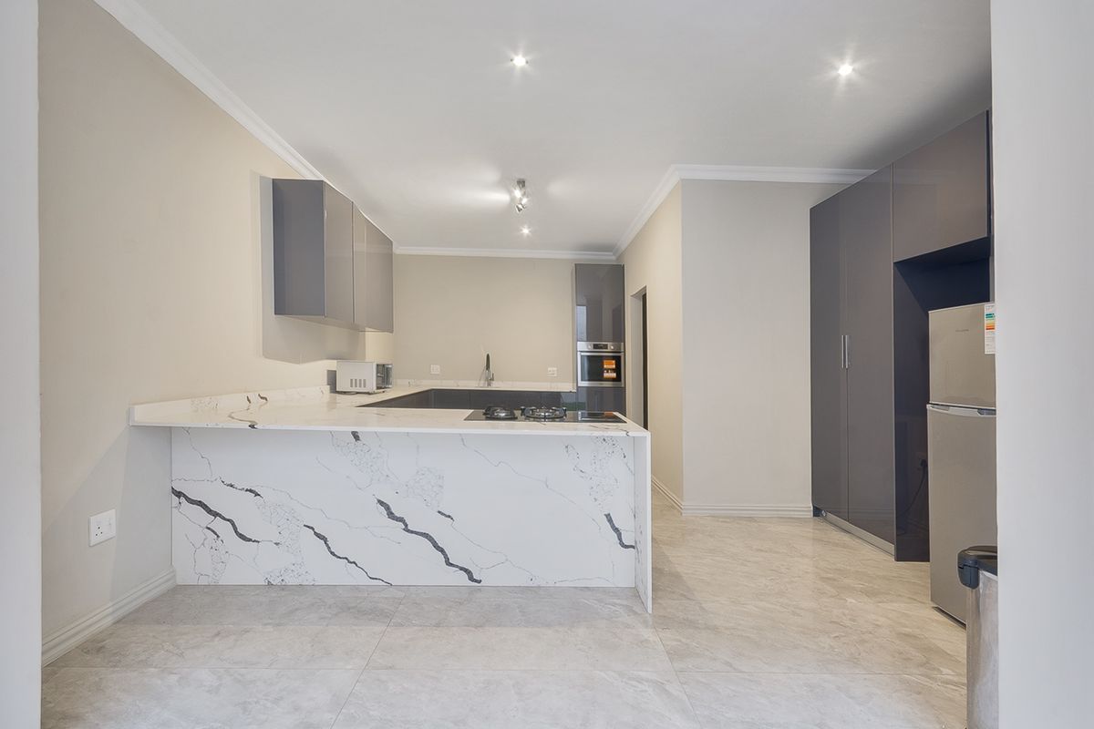 Modern kitchen featuring high-gloss cabinetry, marble-look stone countertops, a built-in oven, and a gas hob, finished with sleek tiled flooring.