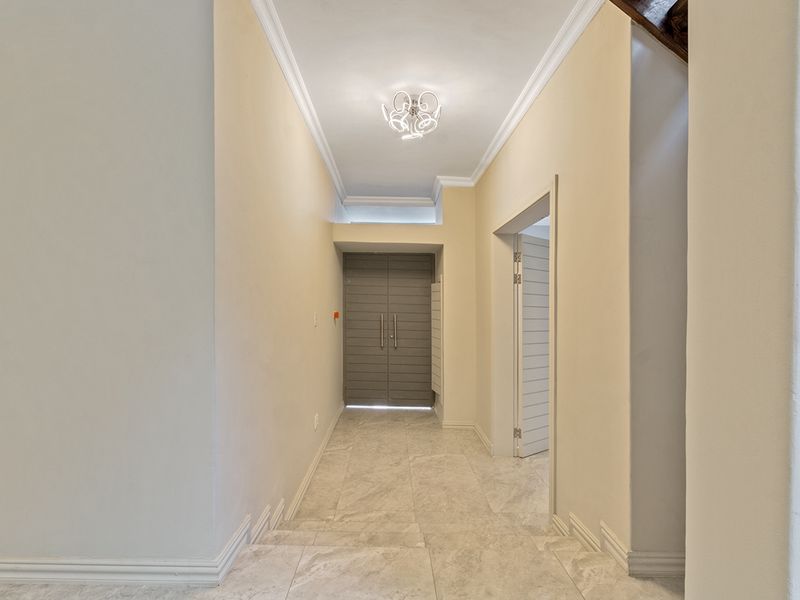A bright and clean entrance hall featuring neutral tiled flooring, crown molding, and double doors leading into the home.