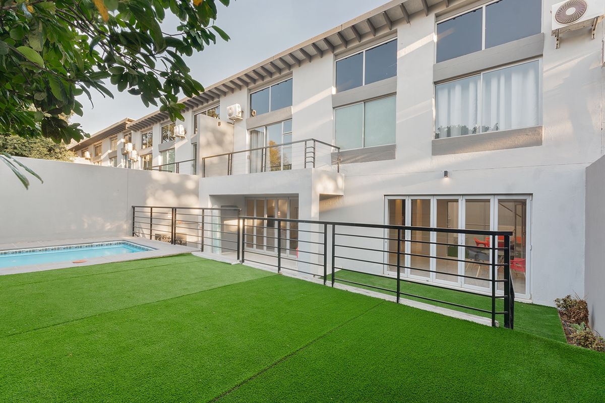 Rear view of the townhouse featuring a private swimming pool, artificial lawn, balcony, and modern sliding glass doors leading to the interior living spaces.