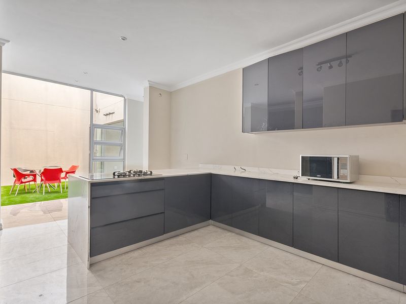 Modern open-plan kitchen featuring sleek grey cabinetry, stone countertops, and a gas hob, seamlessly flowing out to a private patio area.