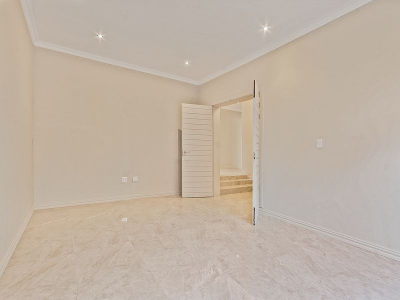A bright, vacant bedroom featuring neutral walls, polished marble-look floor tiles, recessed downlights, and clean architectural finishes.
