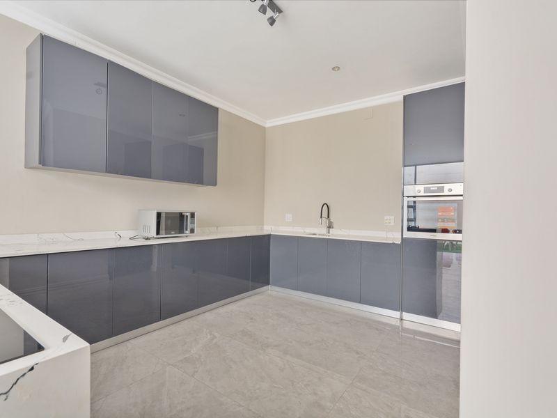 Modern kitchen featuring sleek grey cabinetry, marble-look stone countertops, built-in oven, and high-quality porcelain floor tiles in a clean, contemporary layout.
