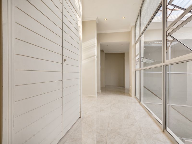 A bright, modern hallway featuring tiled flooring, built-in storage cupboards, and a large glass wall providing natural light.