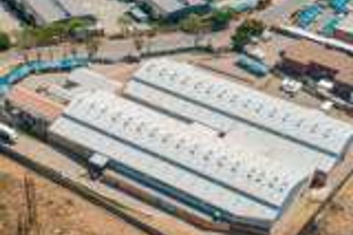 Aerial view of an industrial warehouse property featuring a large metal roof, perimeter fencing, and paved yard space within an industrial park setting.