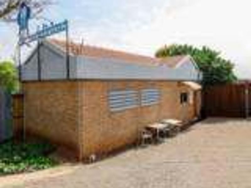 Exterior view of a single-story industrial brick building featuring a tiled roof, louvre windows, and a paved driveway area.