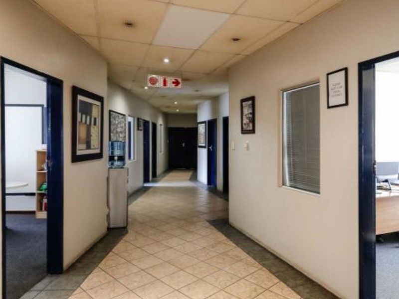A functional industrial office hallway featuring tiled flooring, a suspended ceiling with recessed lighting, and multiple access points to adjacent office spaces.