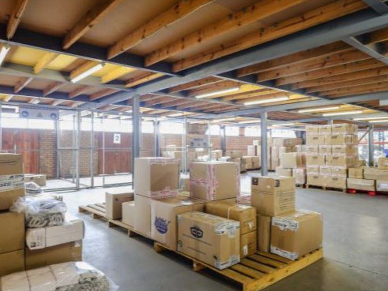 Industrial warehouse space featuring exposed timber ceiling beams, steel structural columns, concrete flooring, and wire mesh partitioning for secure storage areas.