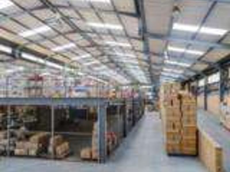 Spacious industrial warehouse featuring a steel portal frame, mezzanine storage level, concrete flooring, and ample natural light through roof skylights.