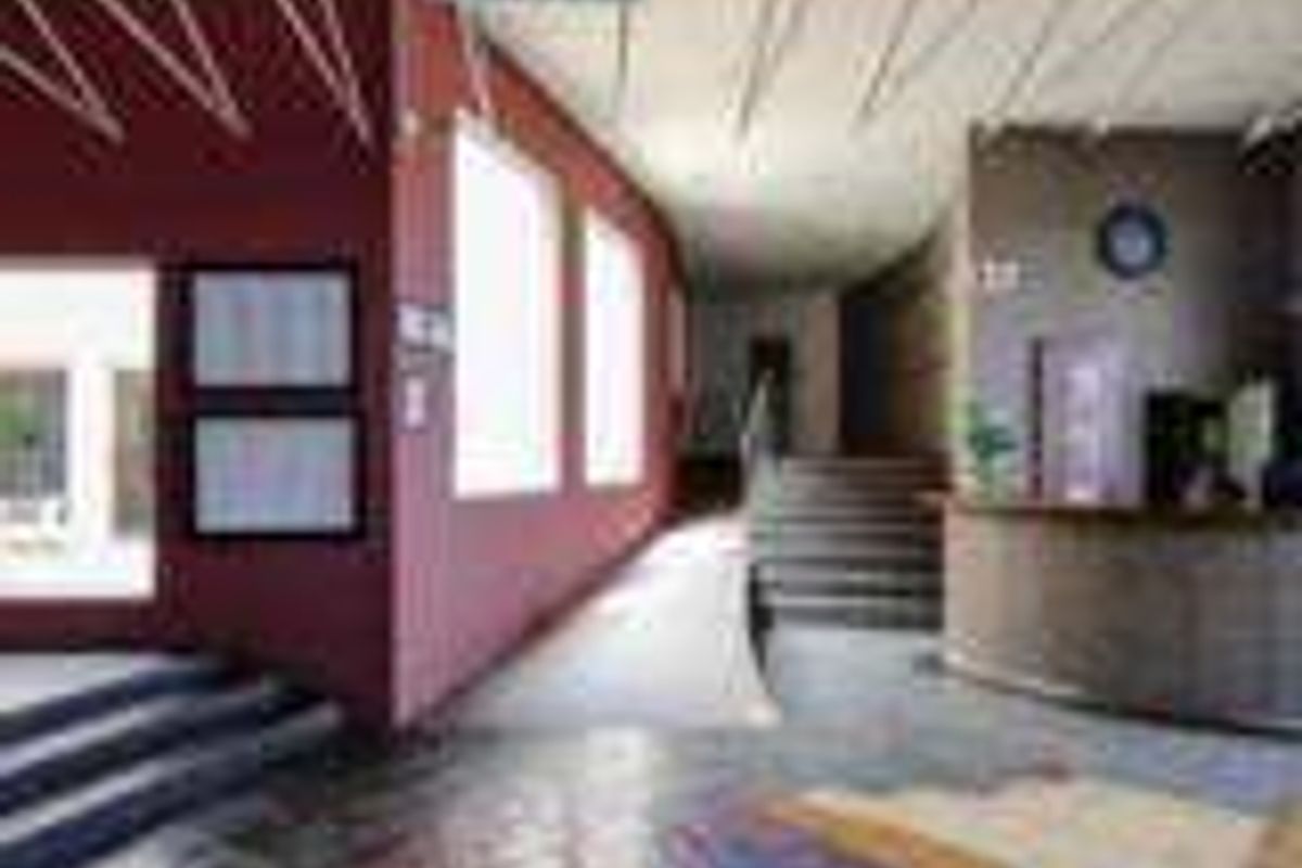 Spacious industrial building entrance featuring a reception desk, accessible ramp, staircase, and decorative tiled flooring with clear emergency signage.