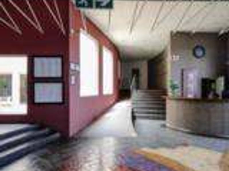Spacious industrial building entrance featuring a reception desk, accessible ramp, staircase, and decorative tiled flooring with clear emergency signage.
