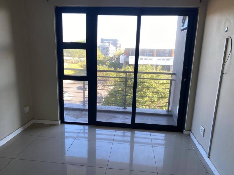 An empty living area featuring large sliding glass doors that open onto a private balcony with a stainless steel railing.
