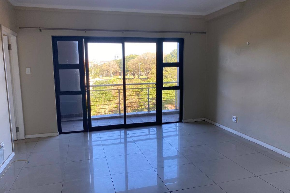 An empty, well-lit living room featuring neutral tiled flooring and large sliding glass doors that provide access to a balcony with scenic views.