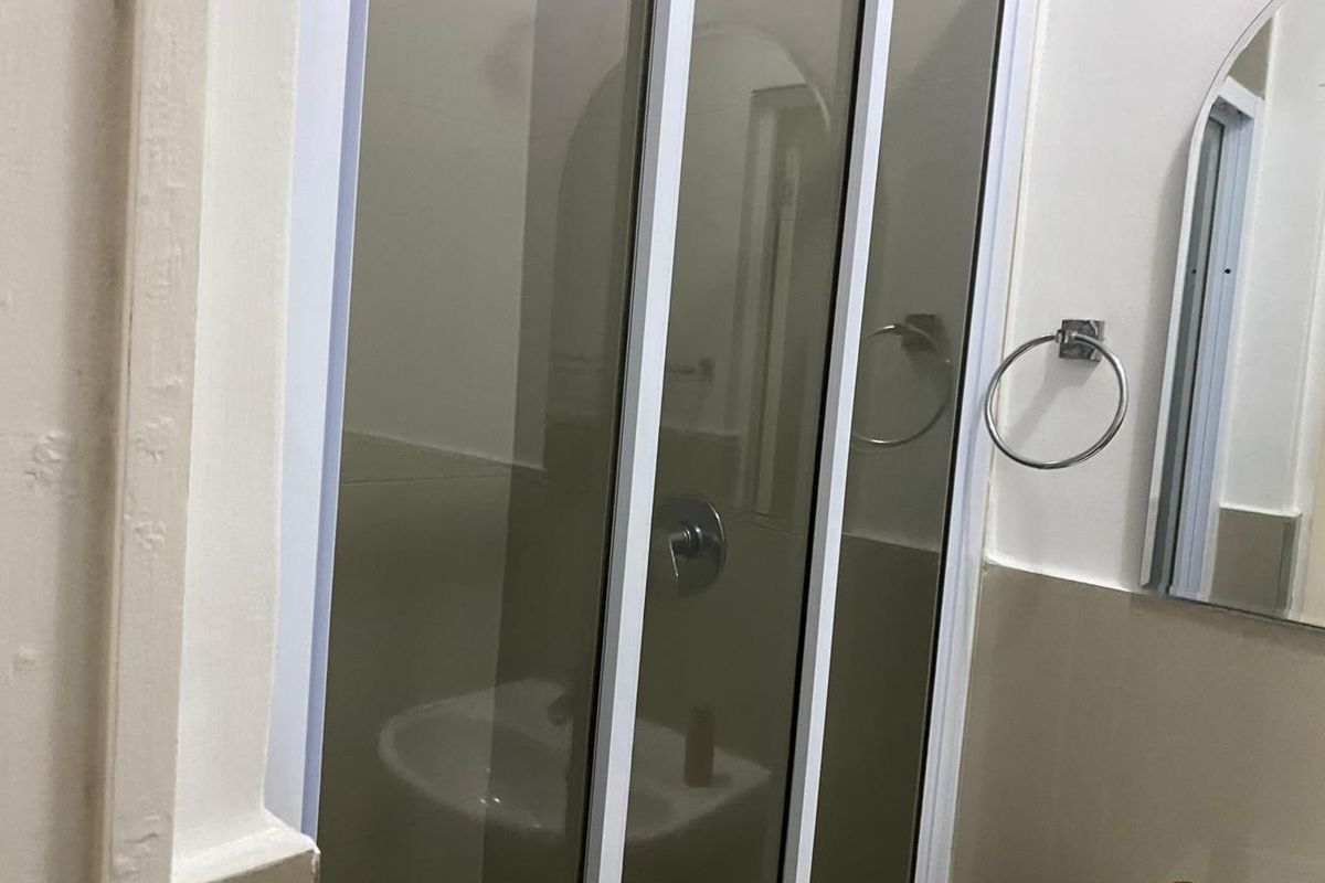 A functional bathroom featuring a shower enclosure, wall-mounted mirror, and chrome fixtures, presenting a clean and simple layout.