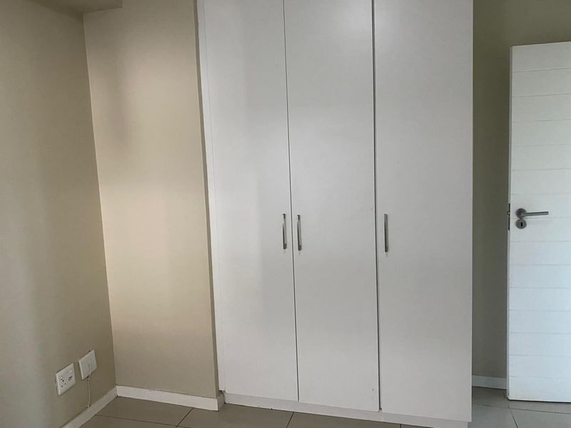 A clean, empty bedroom featuring neutral walls, tiled flooring, and a white built-in wardrobe with modern hardware.