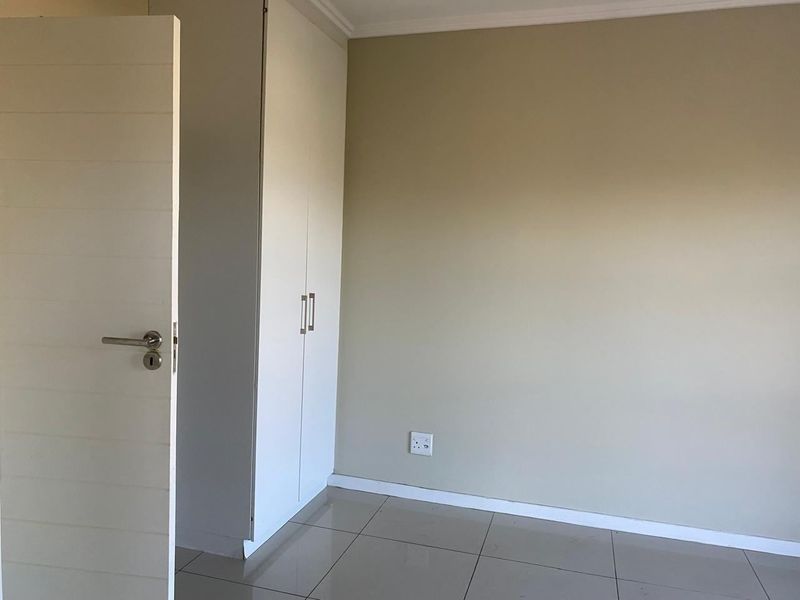 A clean, empty bedroom featuring neutral wall tones, tiled flooring, and a built-in wardrobe.