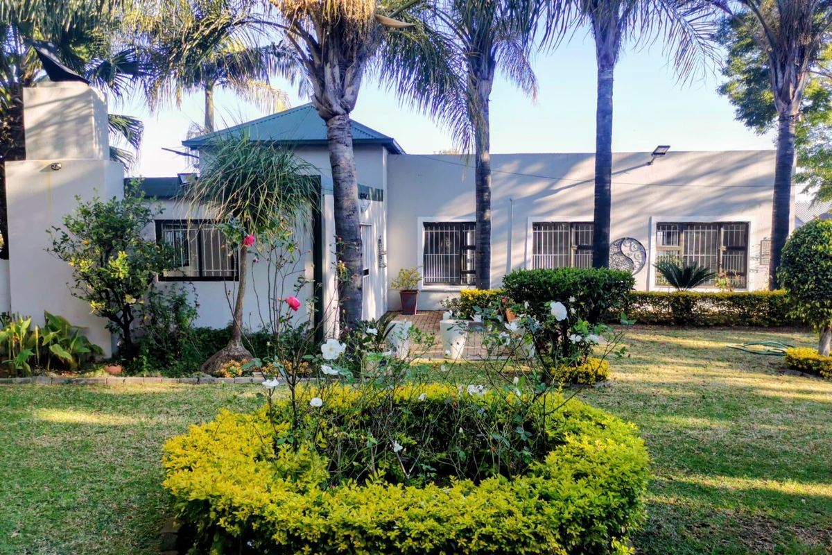 Rear view of the house featuring a landscaped garden, mature palm trees, paved patio area, and external chimney structure.