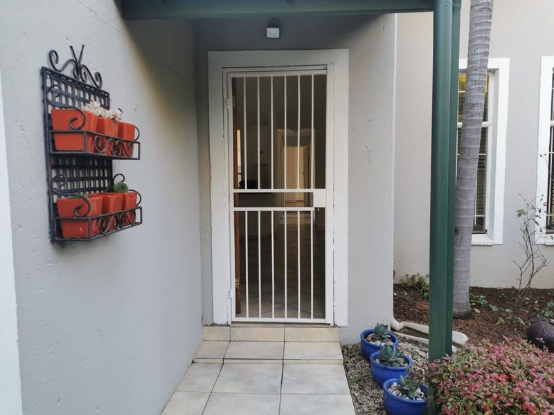 A covered entrance area featuring a white security gate, tiled flooring, and an external wall light.